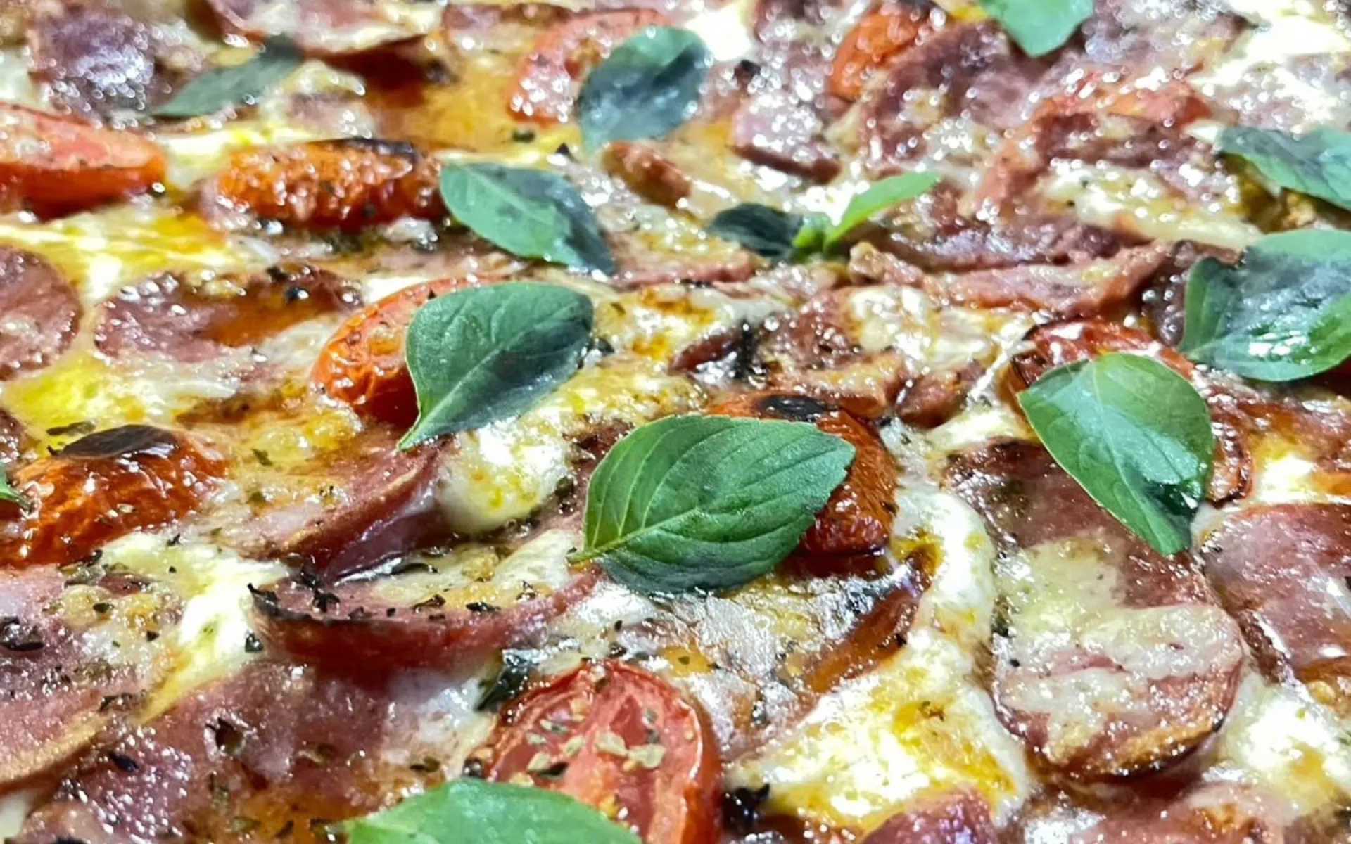 Close de pizza artesanal Italianinha, com manjericão fresco, saindo do forno